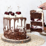 hand pulling a slice of black forest cake from the whole cake
