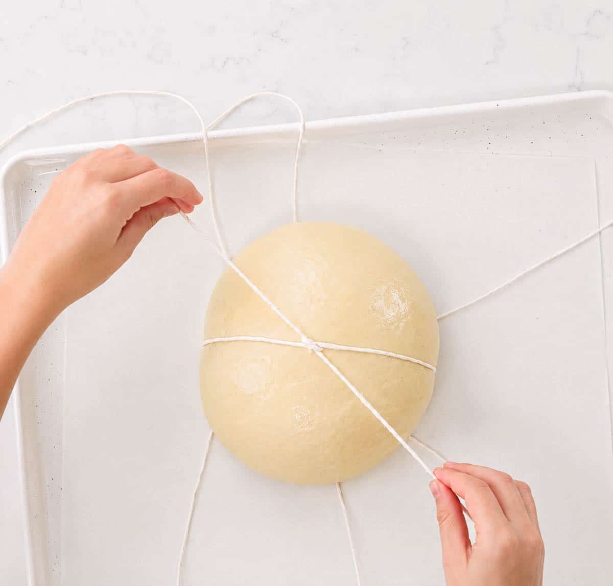 Hands tying bakers twine around a round ball of bread dough.
