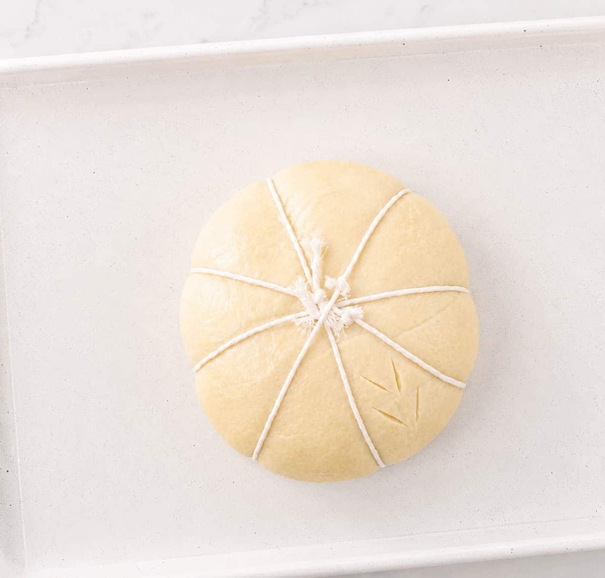Tied bread dough with bakers twine and scored.