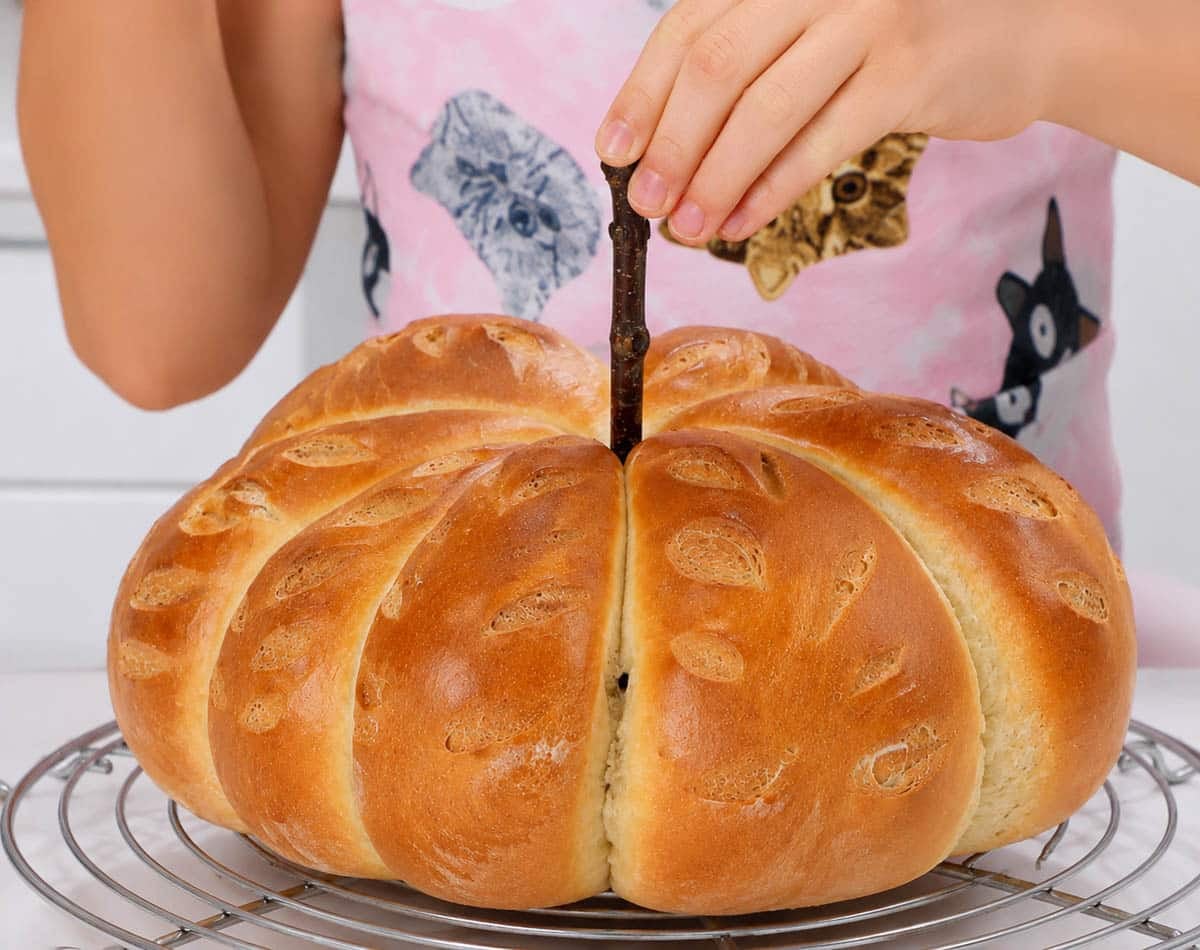 Inserting a stick into pumpkin shaped bread.