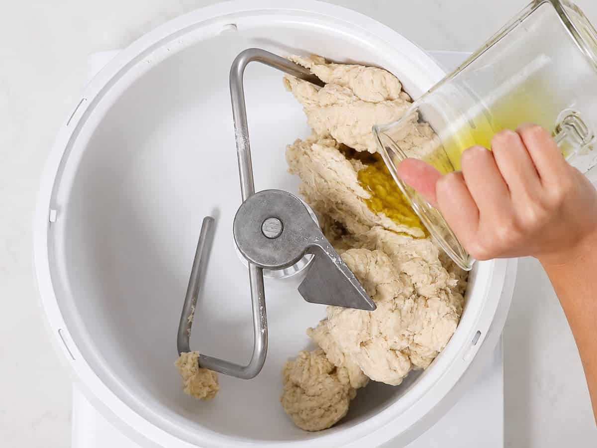 Adding olive oil to bread ingredients in a mixing bowl.