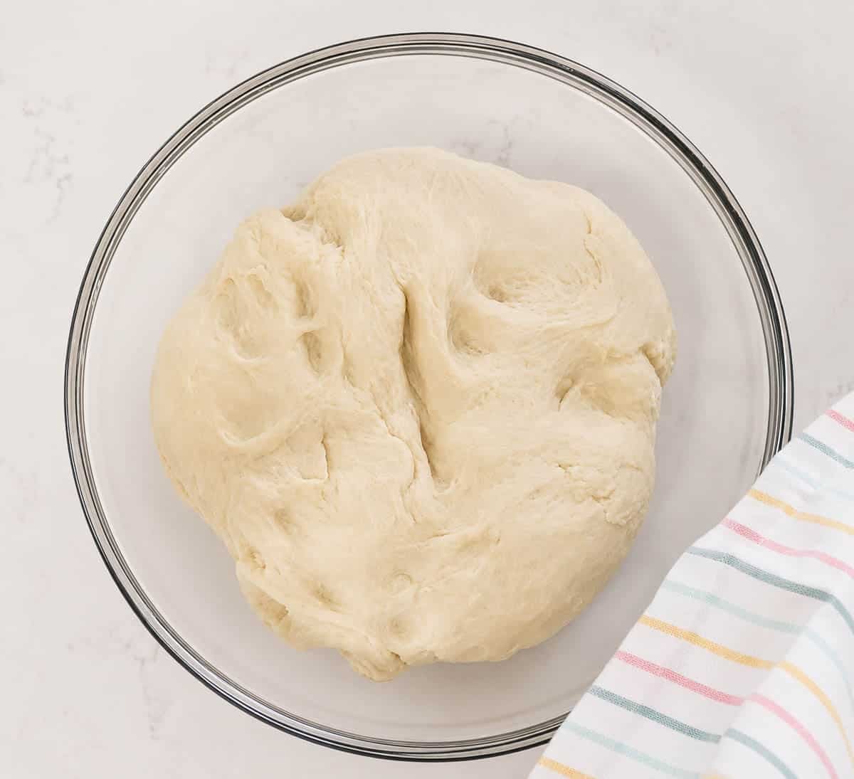 Bread dough in a glass bowl with a towel.