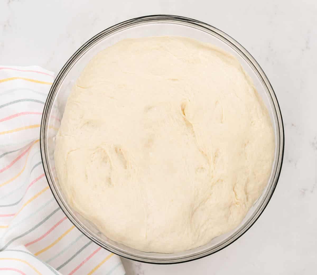 Bread dough proofing in a glass bowl.