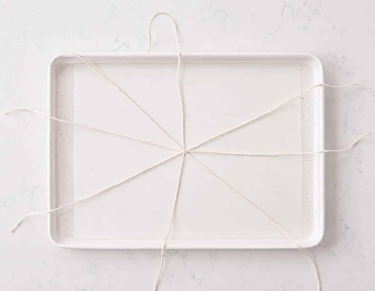 Bakers twine arranged in a criss cross pattern on a sheet pan lined with parchment paper.
