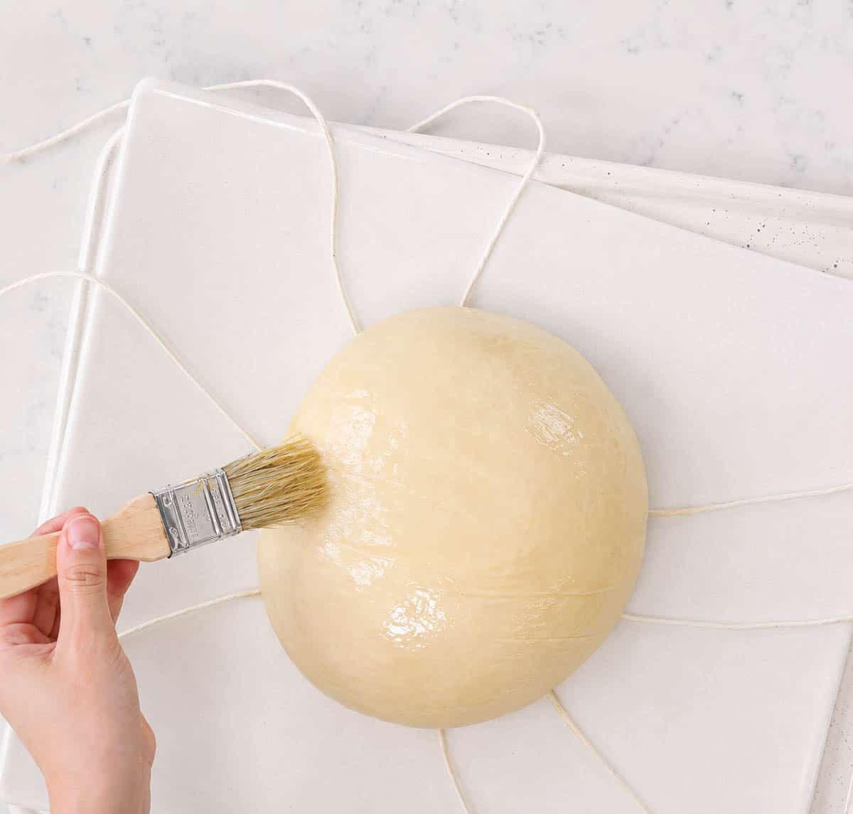 Egg washing bread dough with bakers twine and parchment.