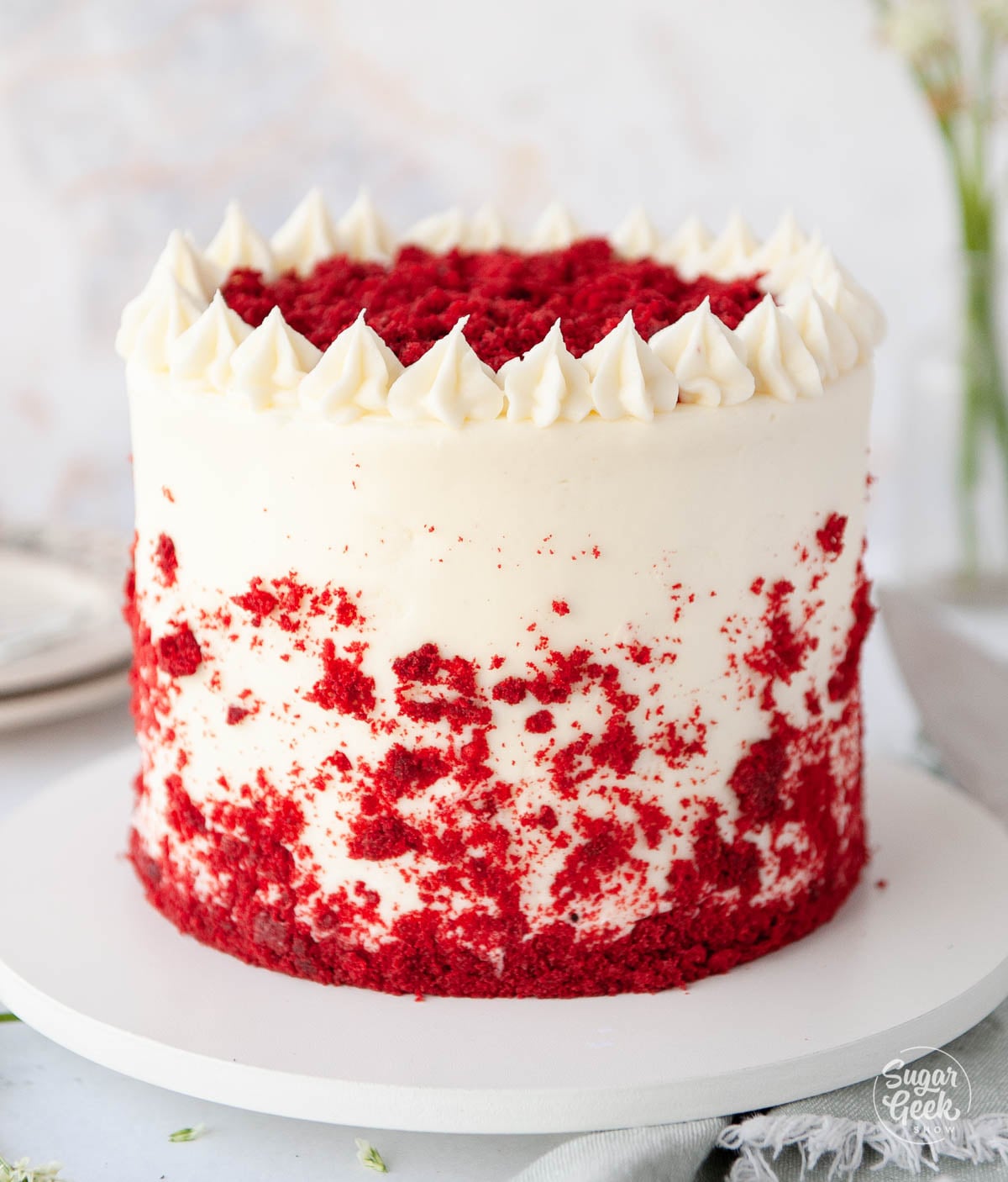 Decorated red velvet cake on a white cake platter.