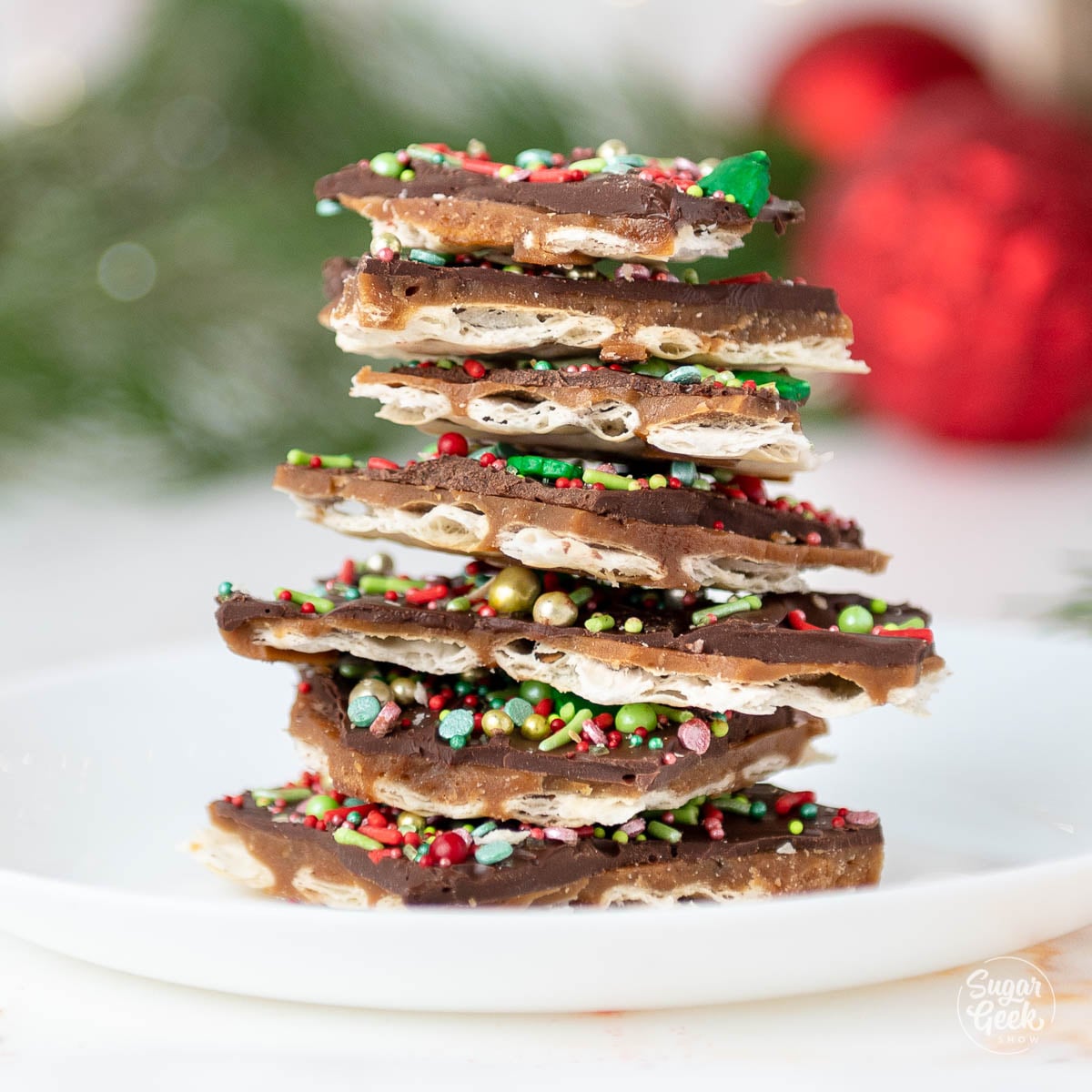 Stack of Christmas crack pieces topped with red and green sprinkles on a white plate.