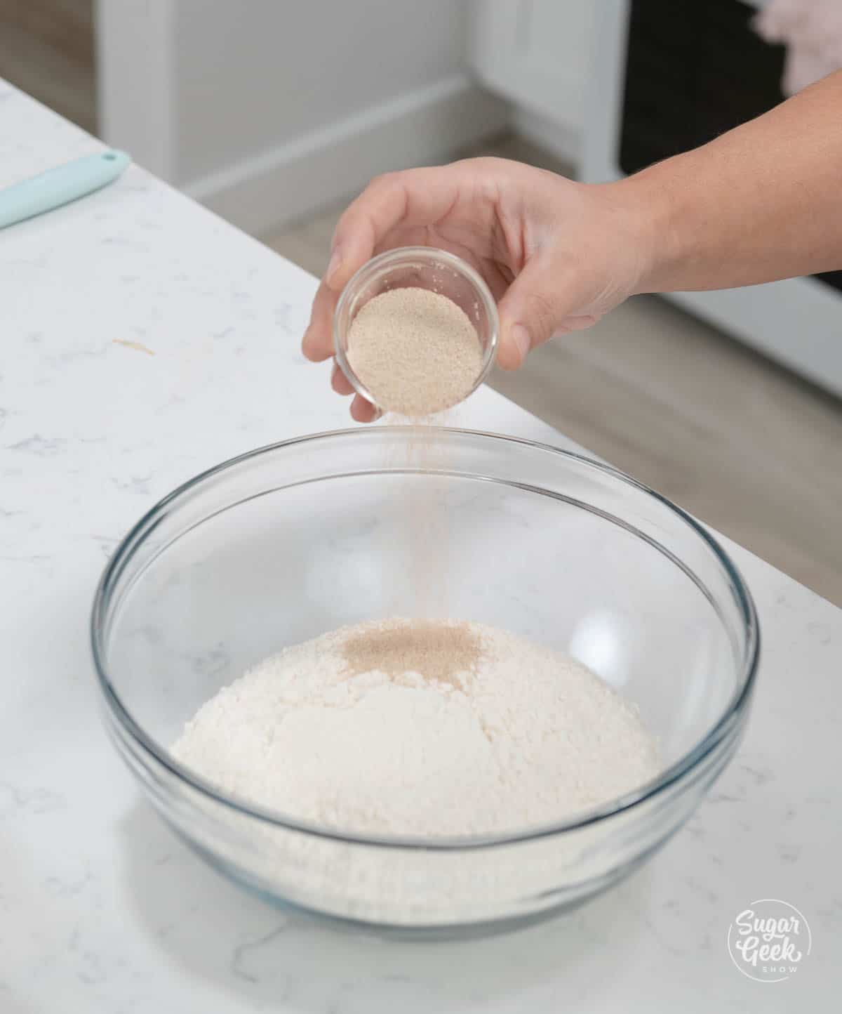 hand holding small bowl of yeast over a bowl of flour