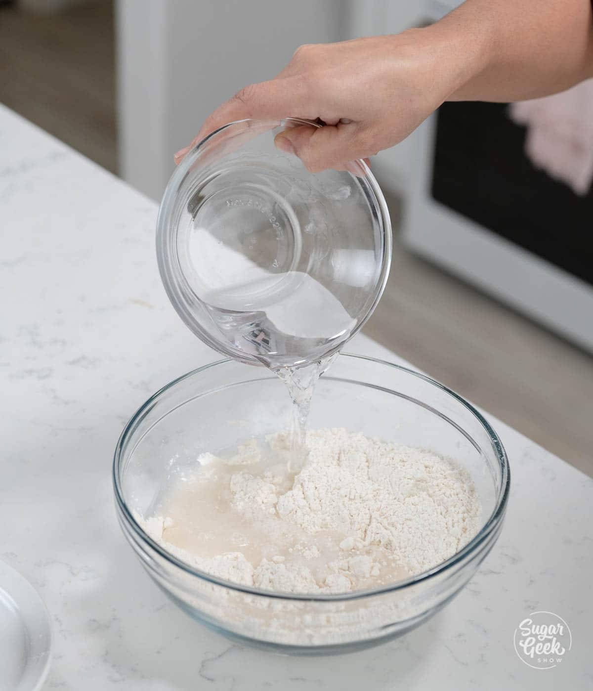 hand holding bowl of water over flour mixture