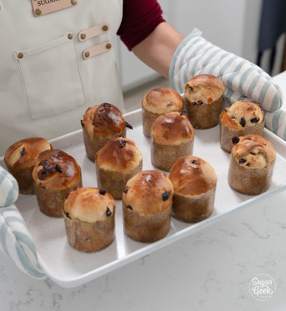 Mini panettone being held on a sheet pan by a woman with oven mitts.