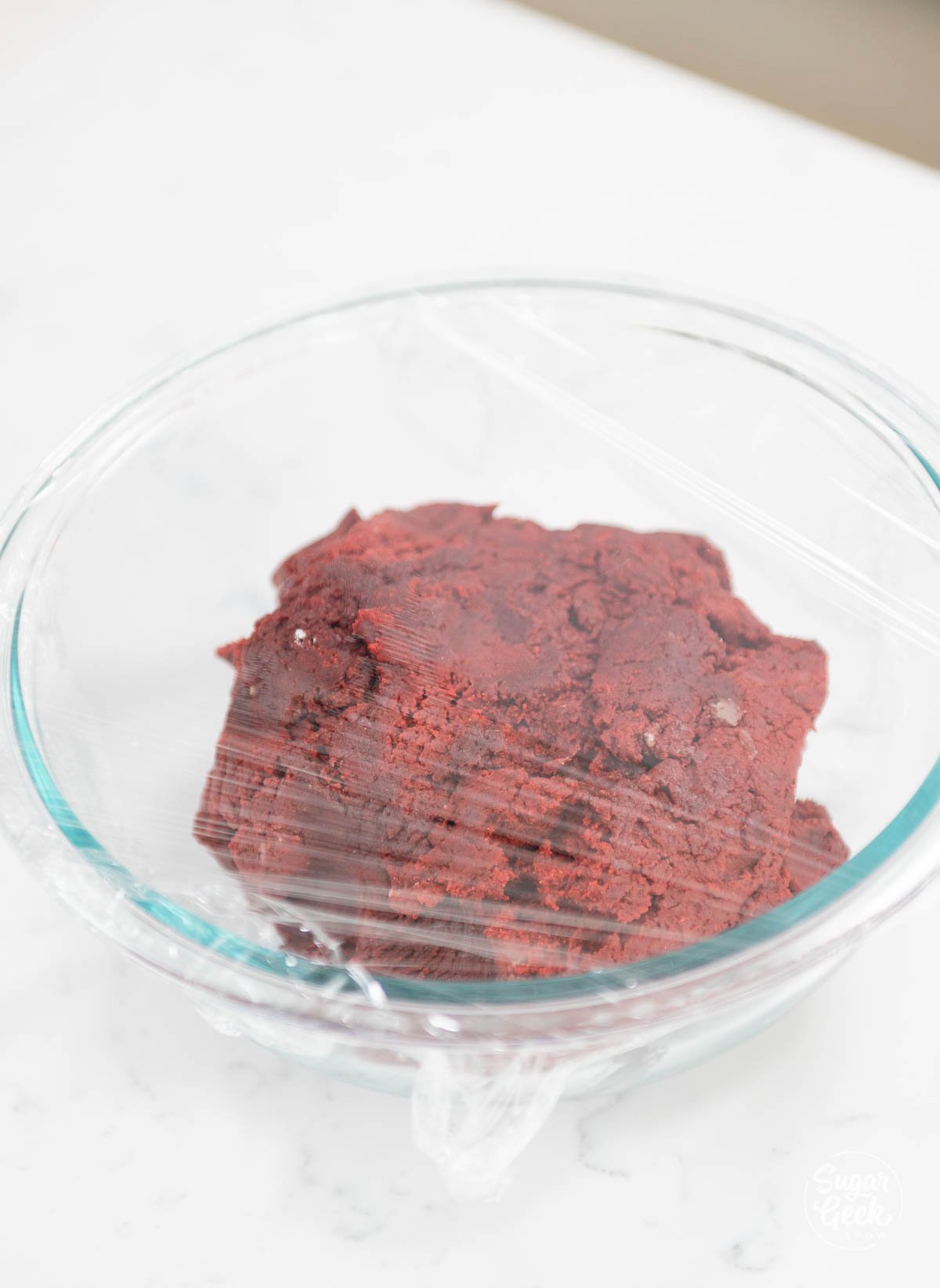 red velvet cookie dough in a clear bowl with clear wrap on top