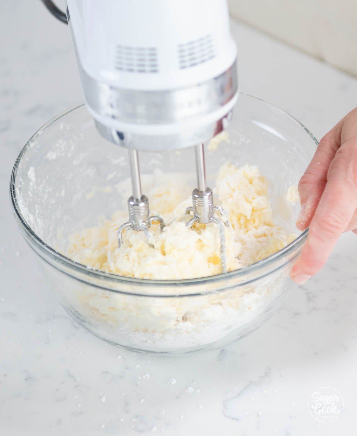 cream cheese filling in a clear bowl with hand mixer