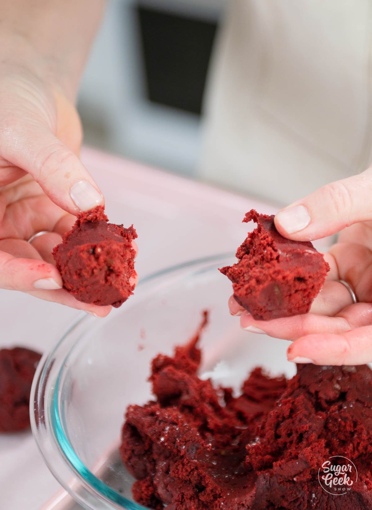 two hands separating red velvet cookie dough into two pieces