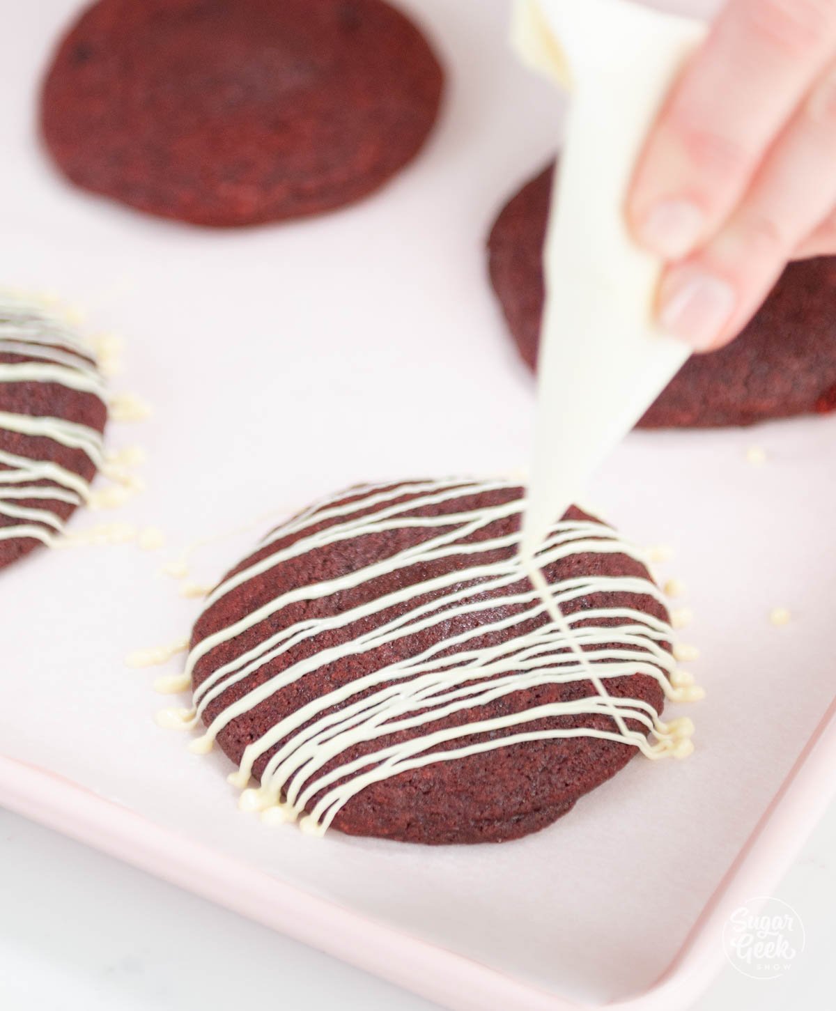 drizzling white chocolate on red velvet cookies