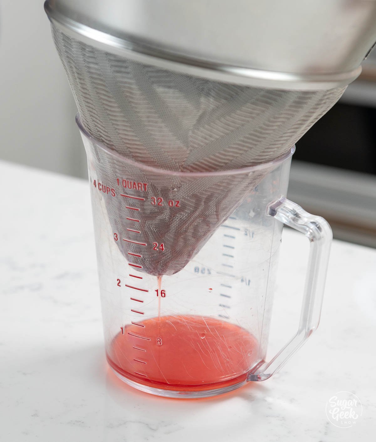 strainer inside of a large measuring cup with strawberry juice dripping