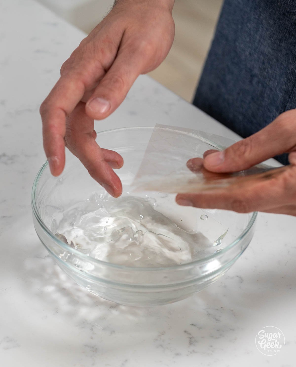hands holding a sheet of gelatin above a bowl of water