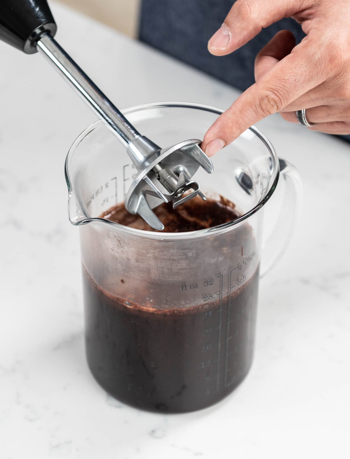 hand pointing to immersion blender above pitcher of chocolate glaze