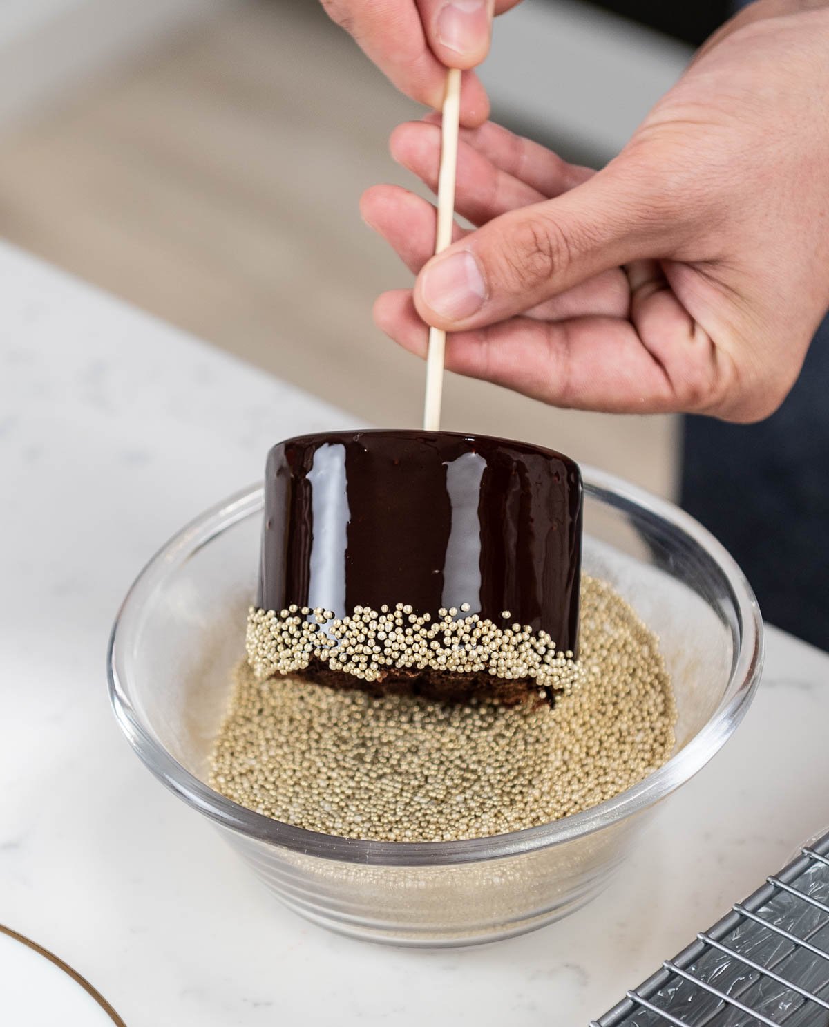 hand rolling chocolate entremet in bowl of edible gold sprinkles
