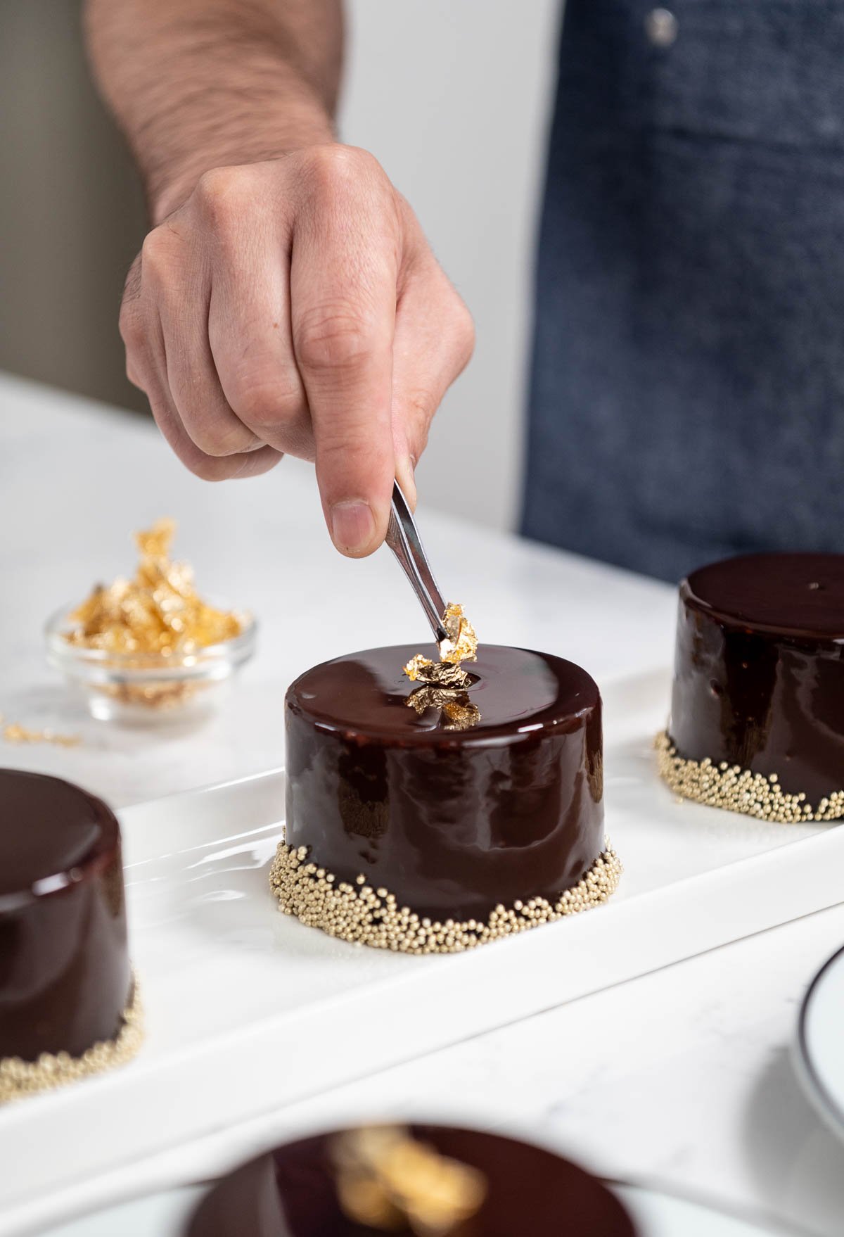 hand placing edible gold on top of chocolate entremet using tweezers