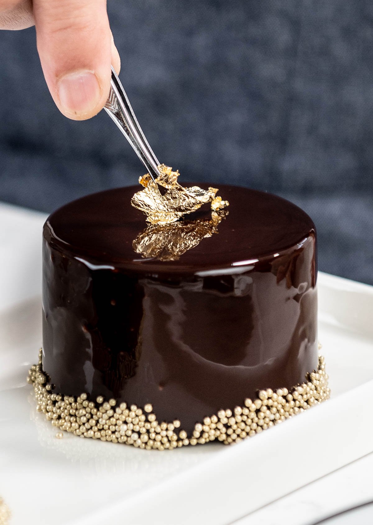 hand placing edible gold on top of chocolate entremet using tweezers