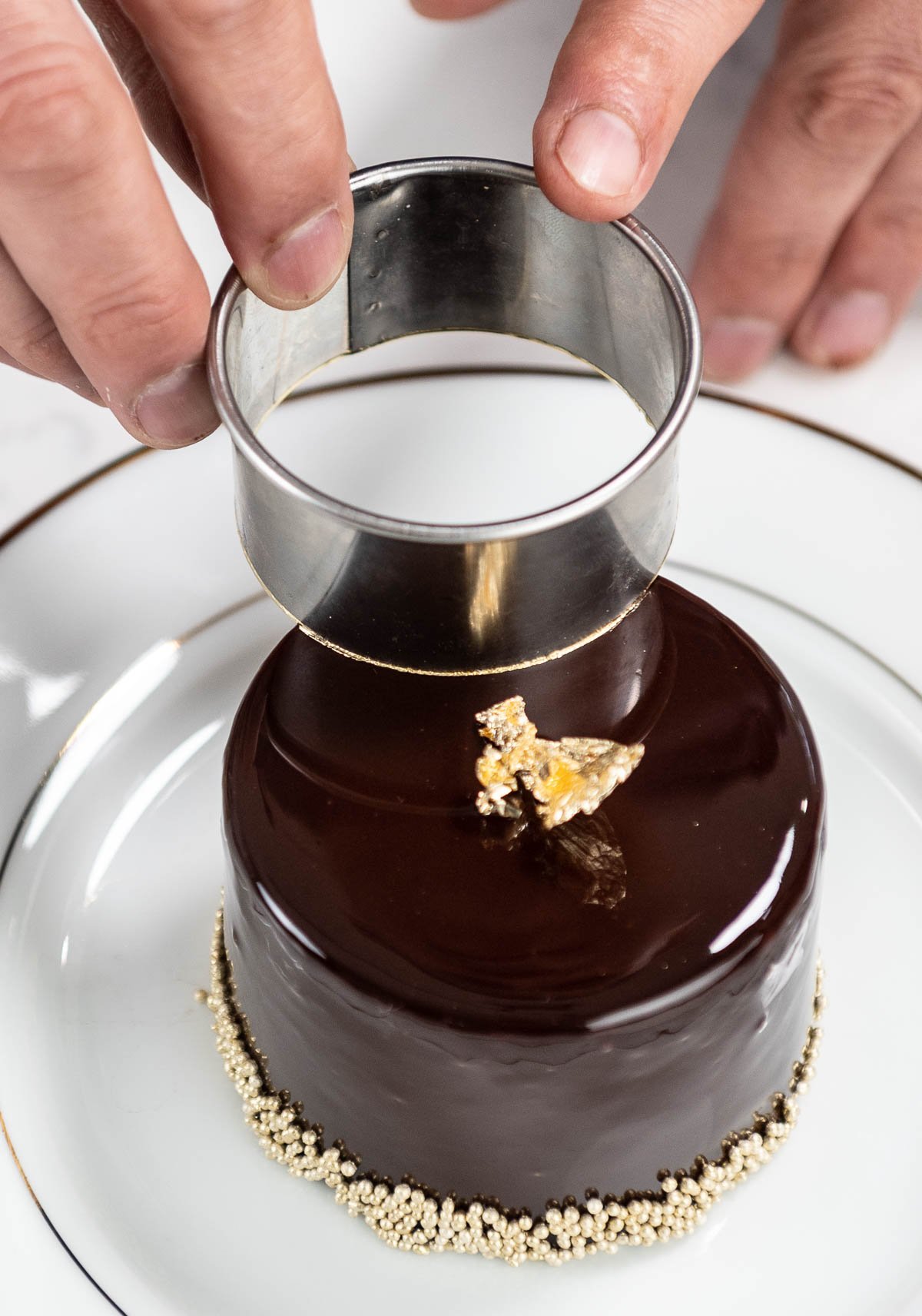 hand adding edible gold decorations to chocolate entremet