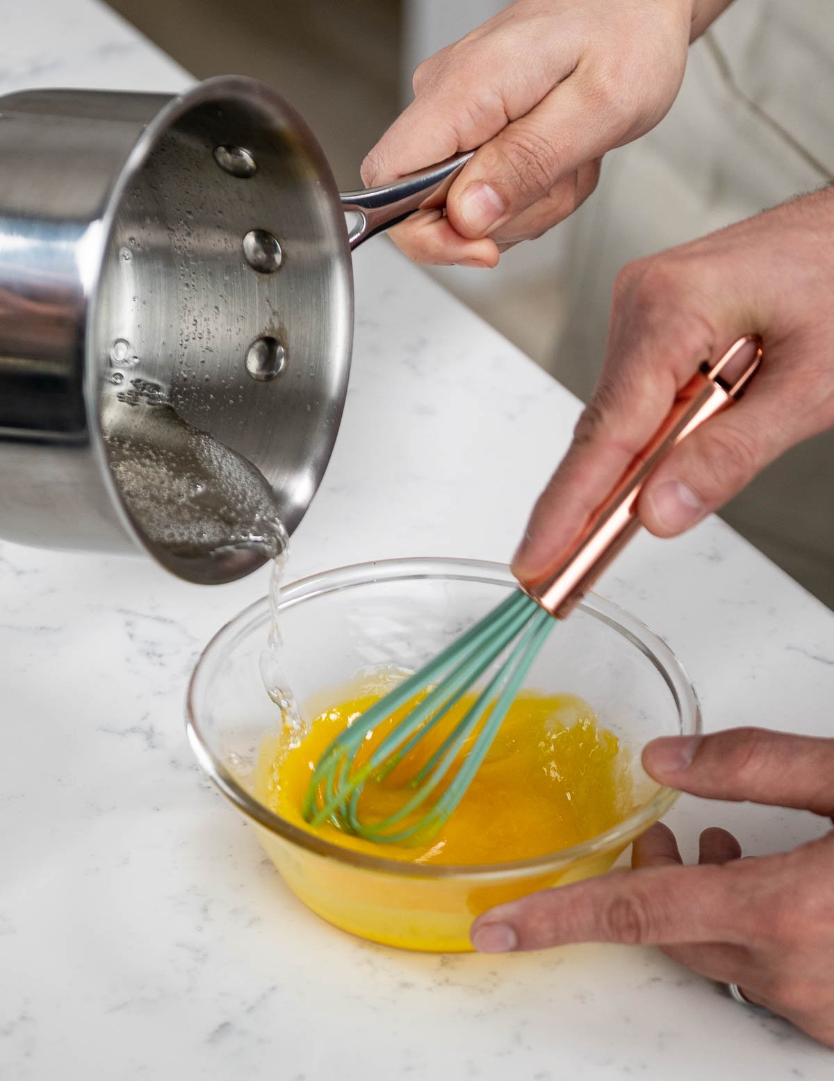 pouring ingredients from saucepan into mixing bowl while whisking