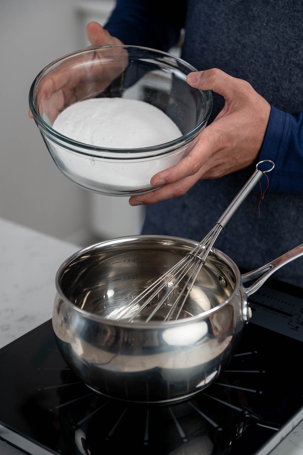 holding bowl of sugar above saucepan