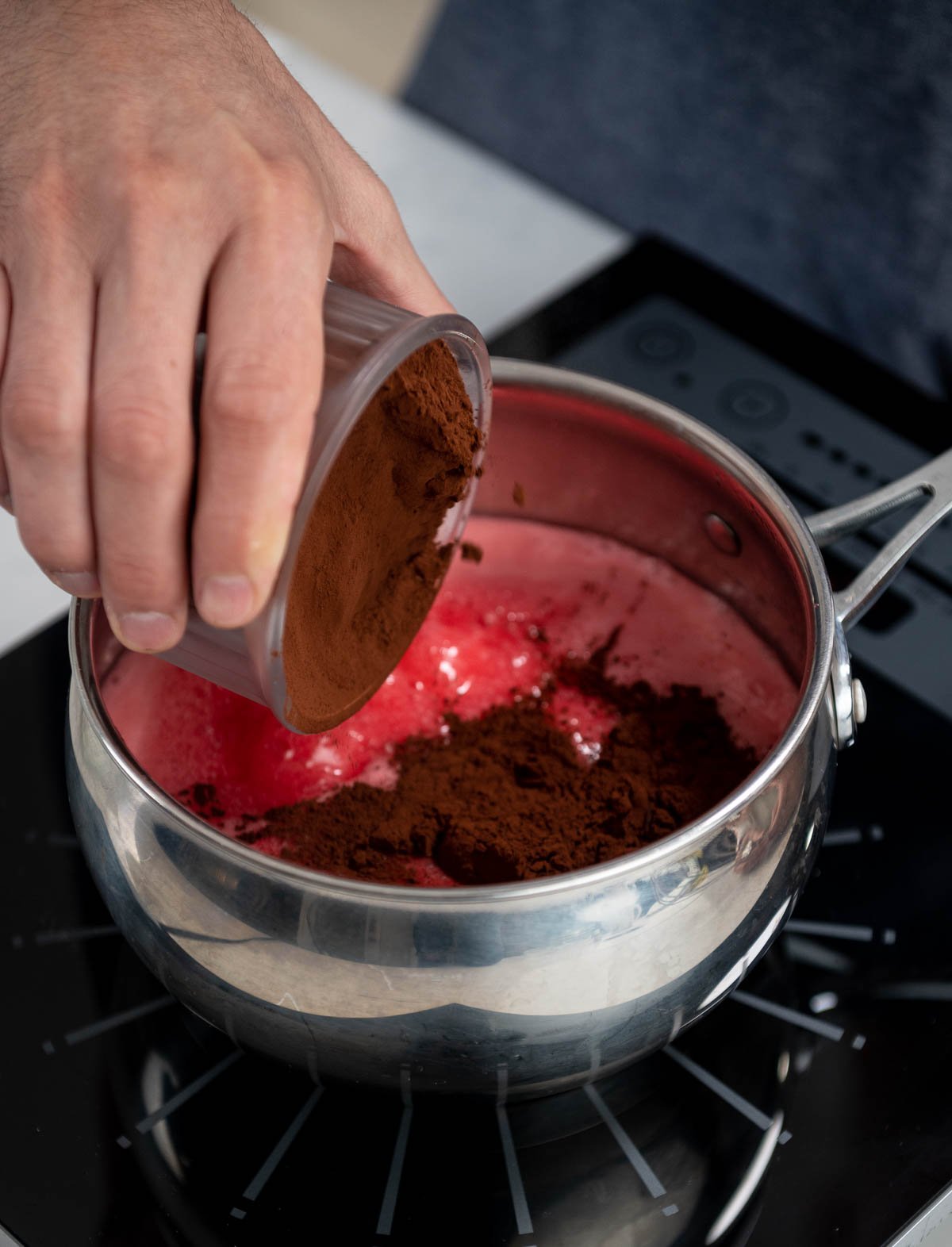 hand pouring cocoa powder into saucepan