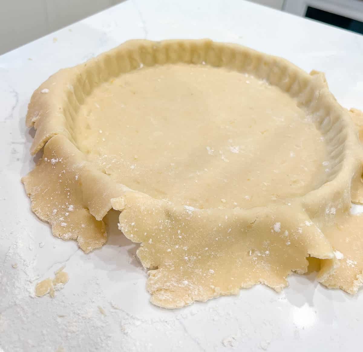 tart dough placed into a tart tin with leftover dough draped over the sides