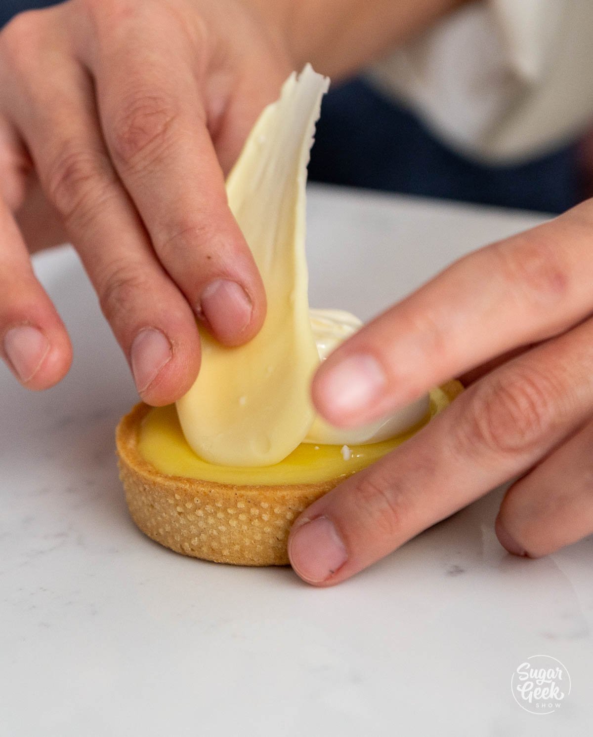 hand placing white chocolate on lemon tart