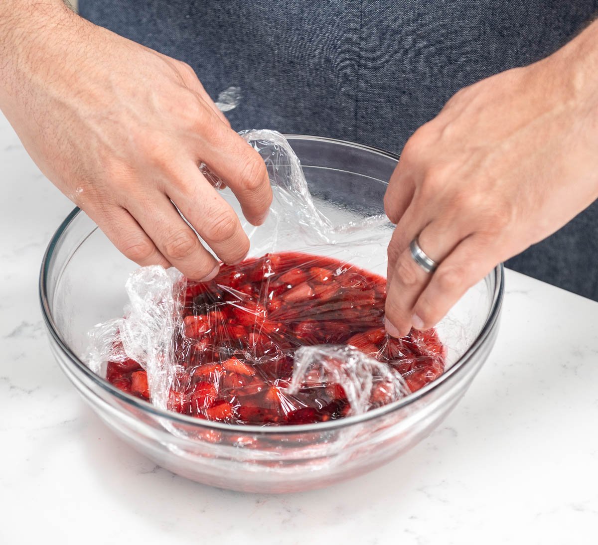 placing plastic wrap on top of berry sauce in bowl