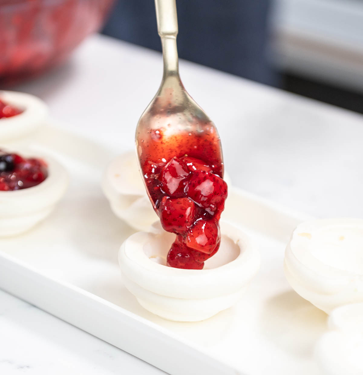 spoon pouring berry compote into mini pavlova shell