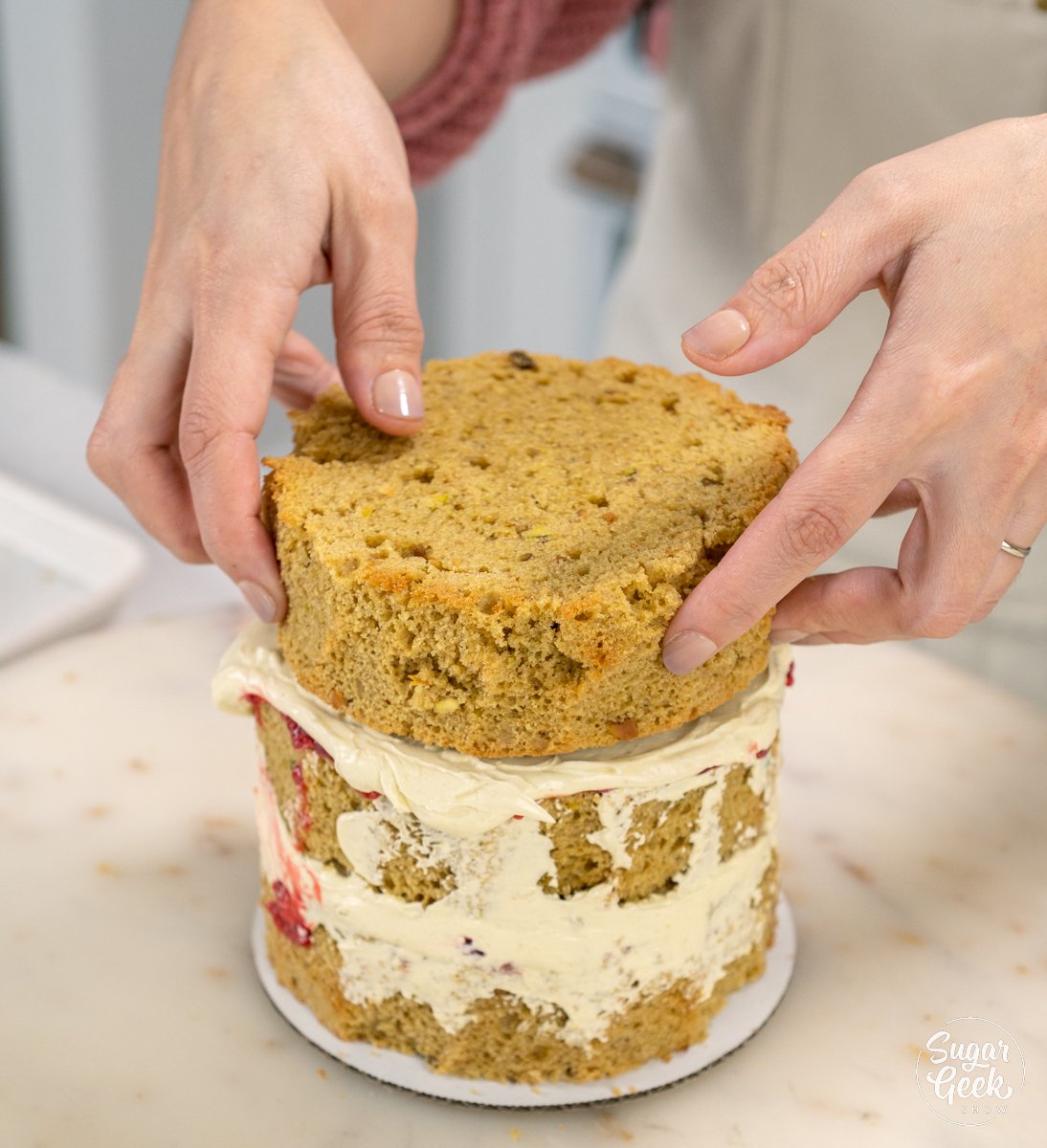 adding the top layer of cake to the pistachio cake