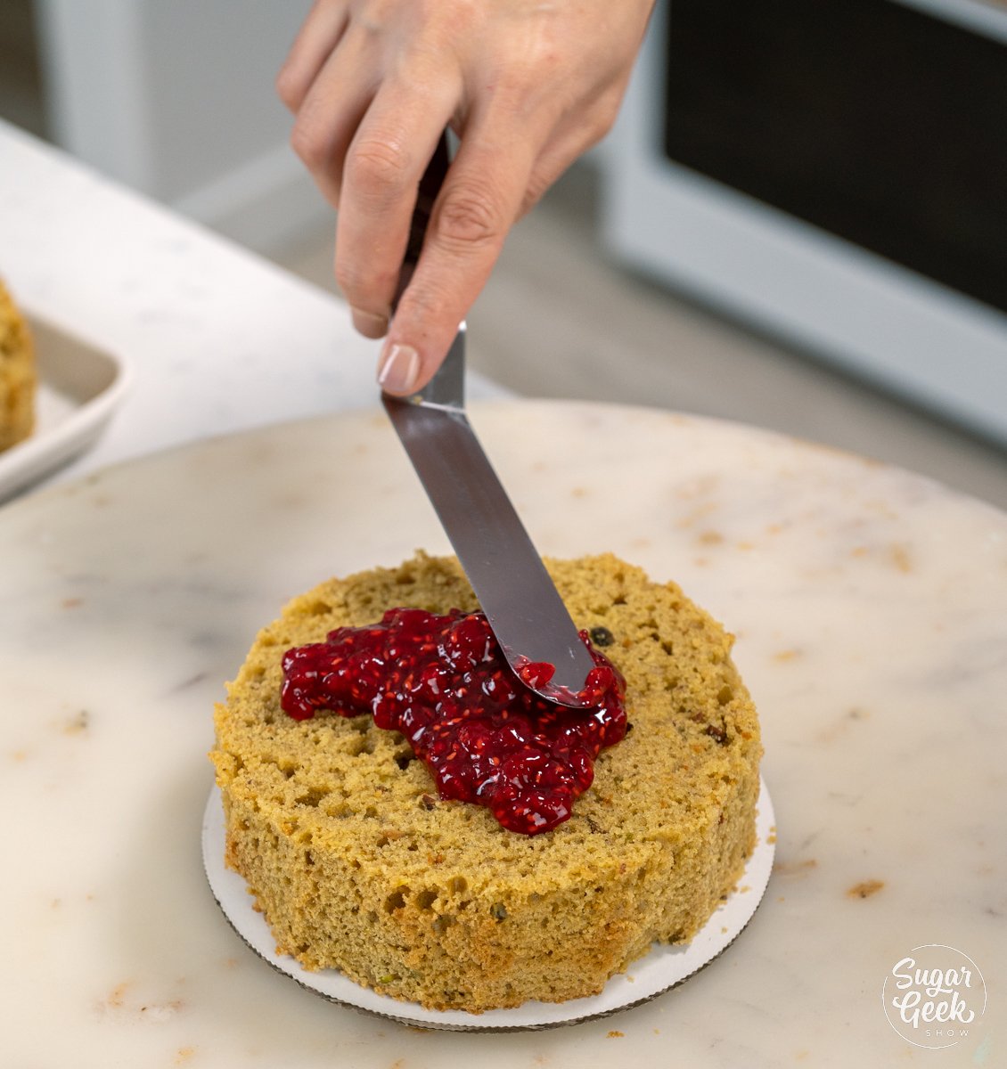 adding raspberry filling to pistachio cake layer