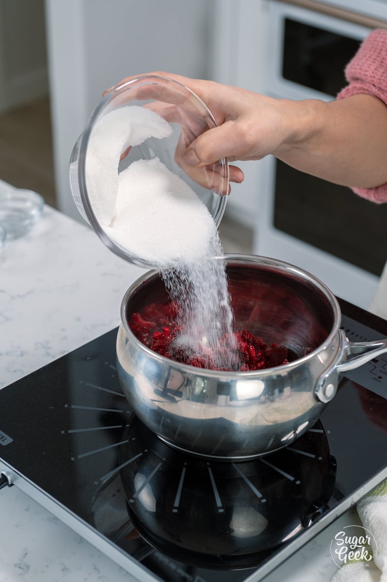 pouring sugar onto raspberries in a saucepan