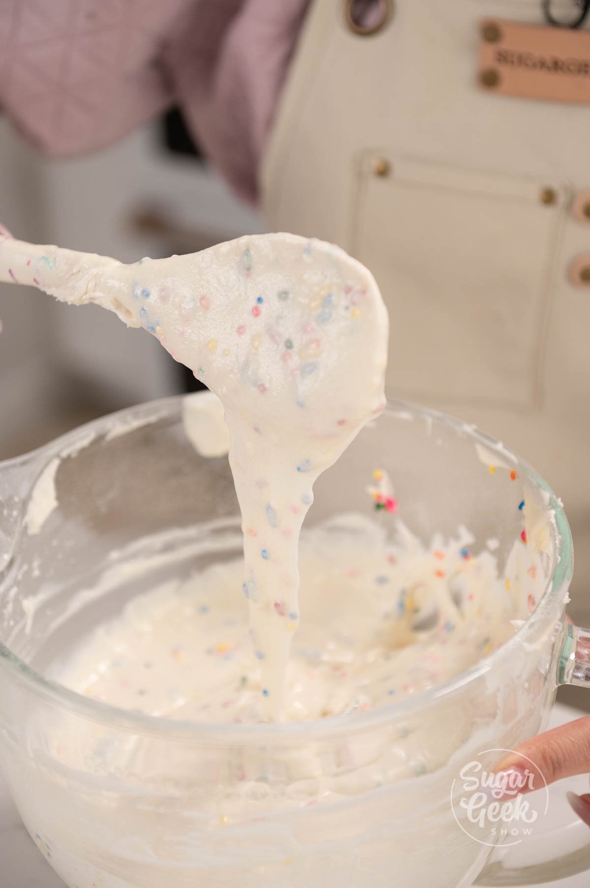spatula being held above mixing bowl covered in cake batter with sprinkles