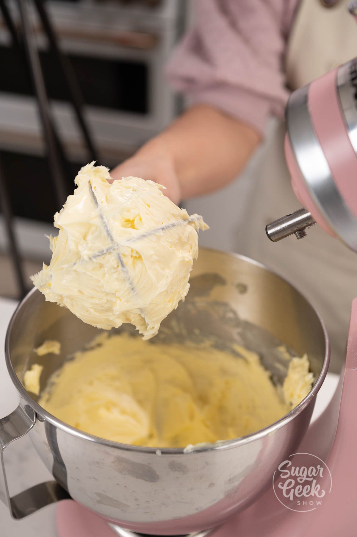 hand holding whisk covered in whipped butter above mixing bowl.