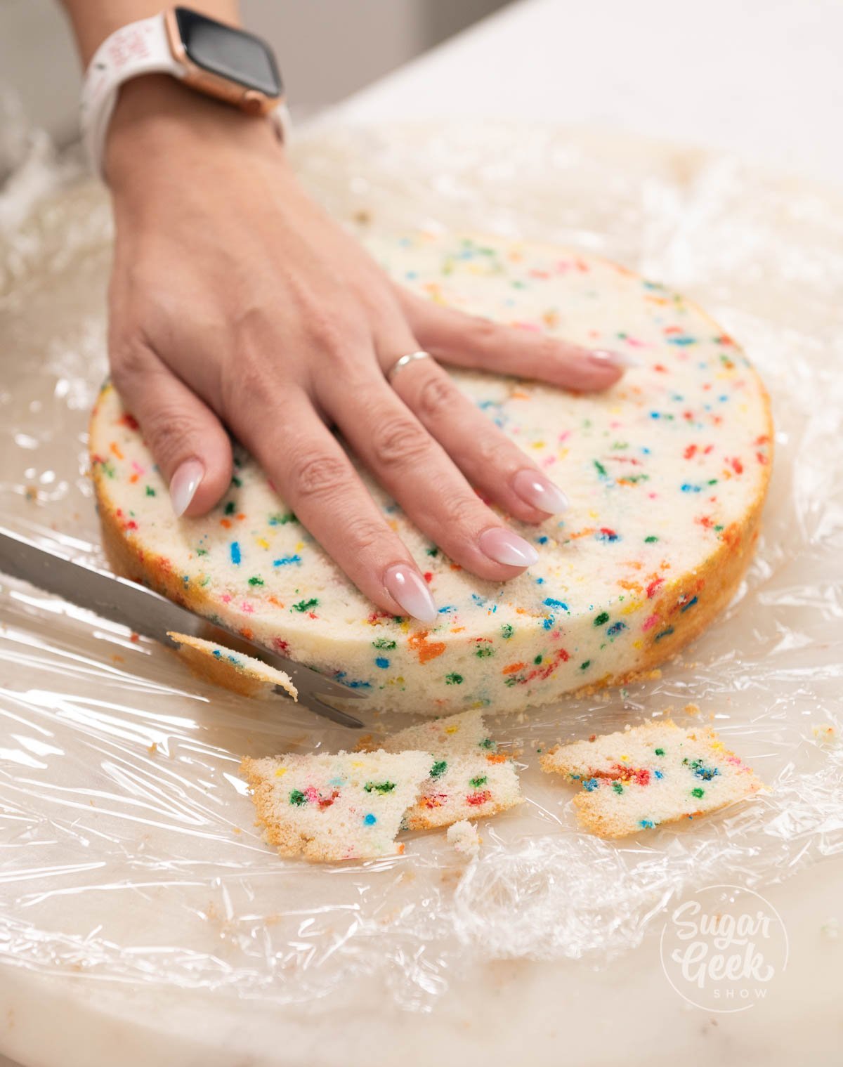 hand on top of cake layer holding knife while cutting cake