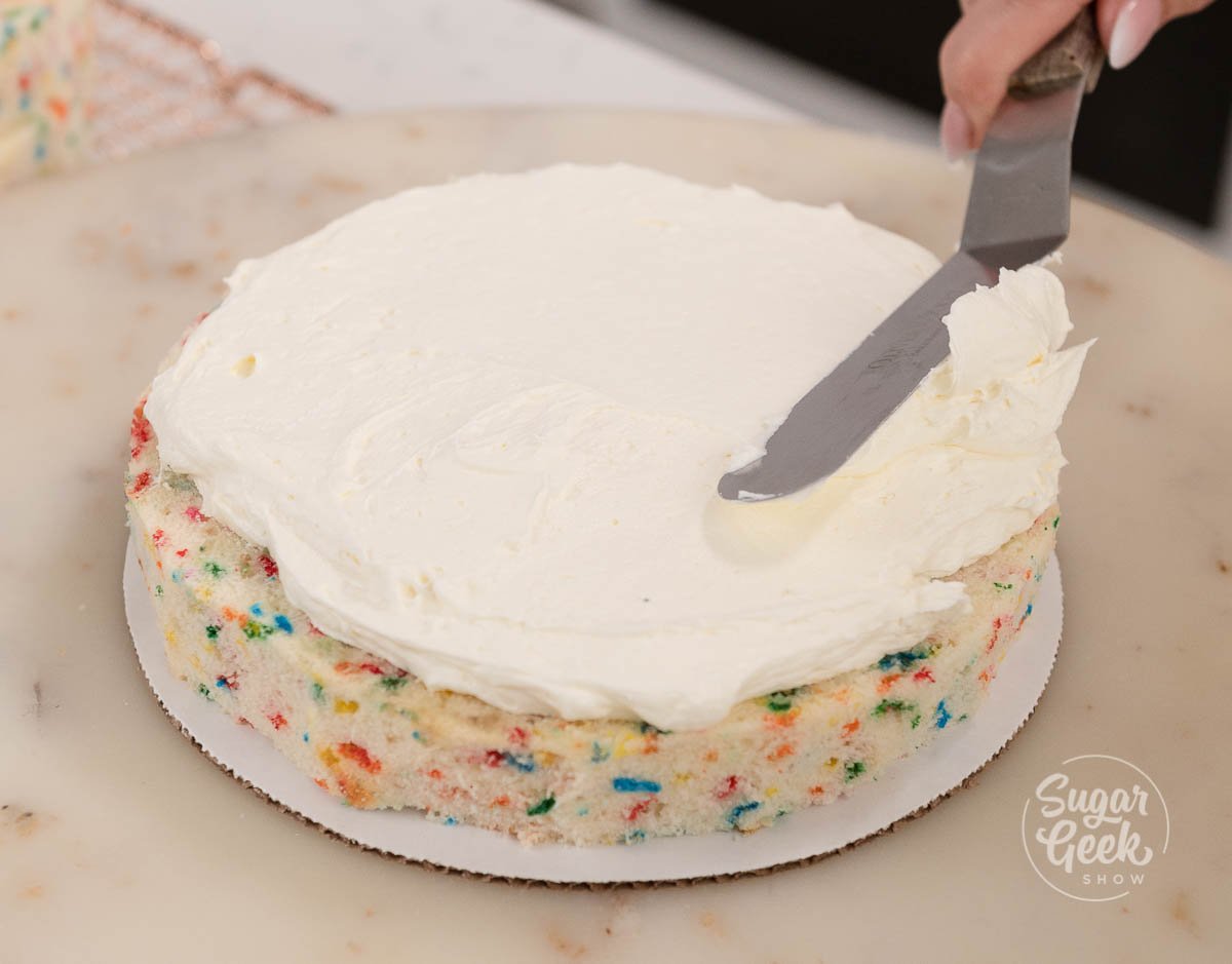 hand holding spatula while icing a cake layer