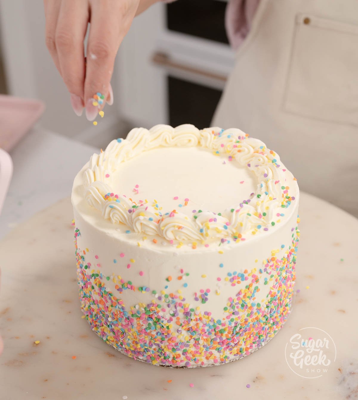 hand placing sprinkles on top of decorated cake.