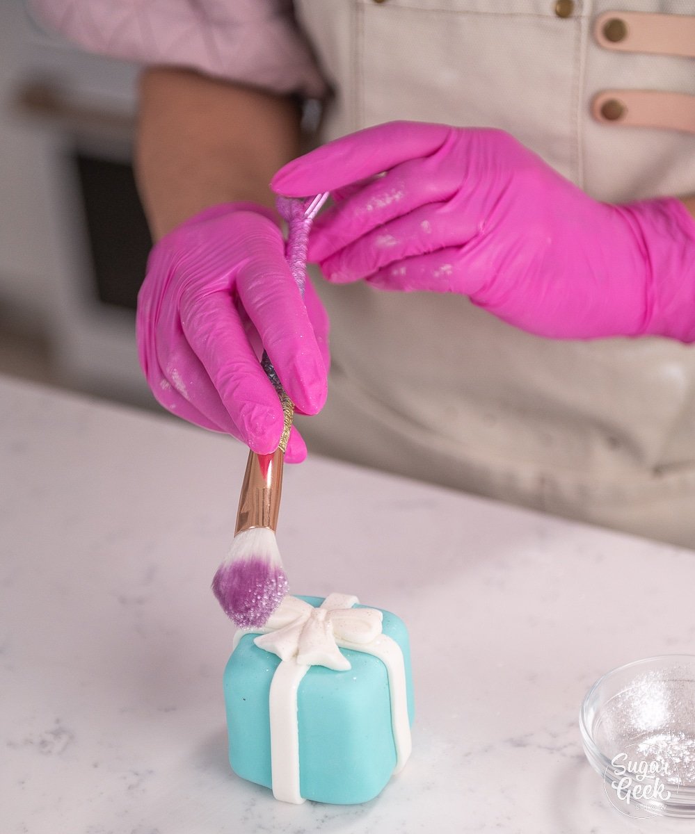 hand sprinkling edible glitter onto a cake using a brush
