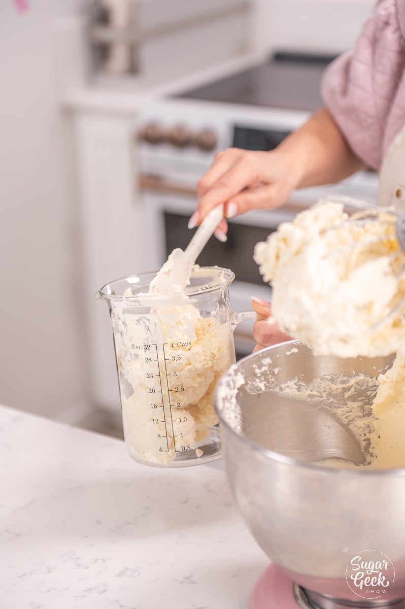 hand scooping frosting into large, tall measuring cup