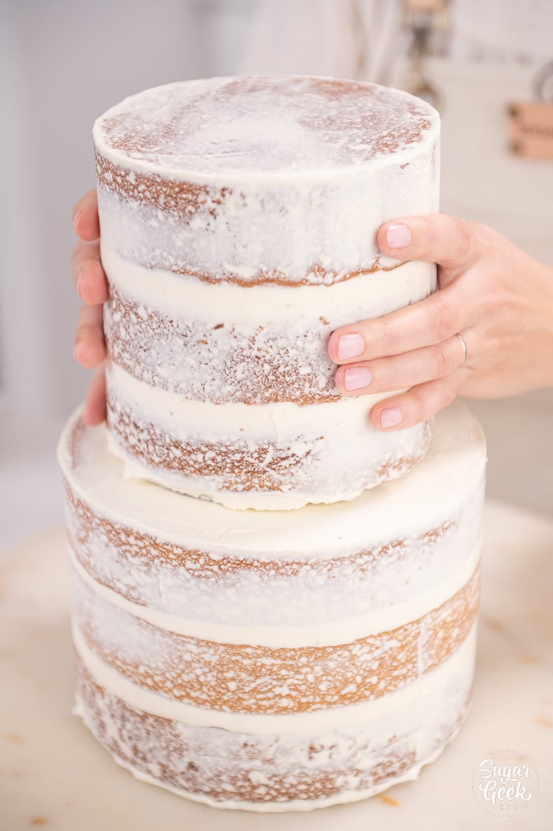 hands placing cake tiers on top of cake