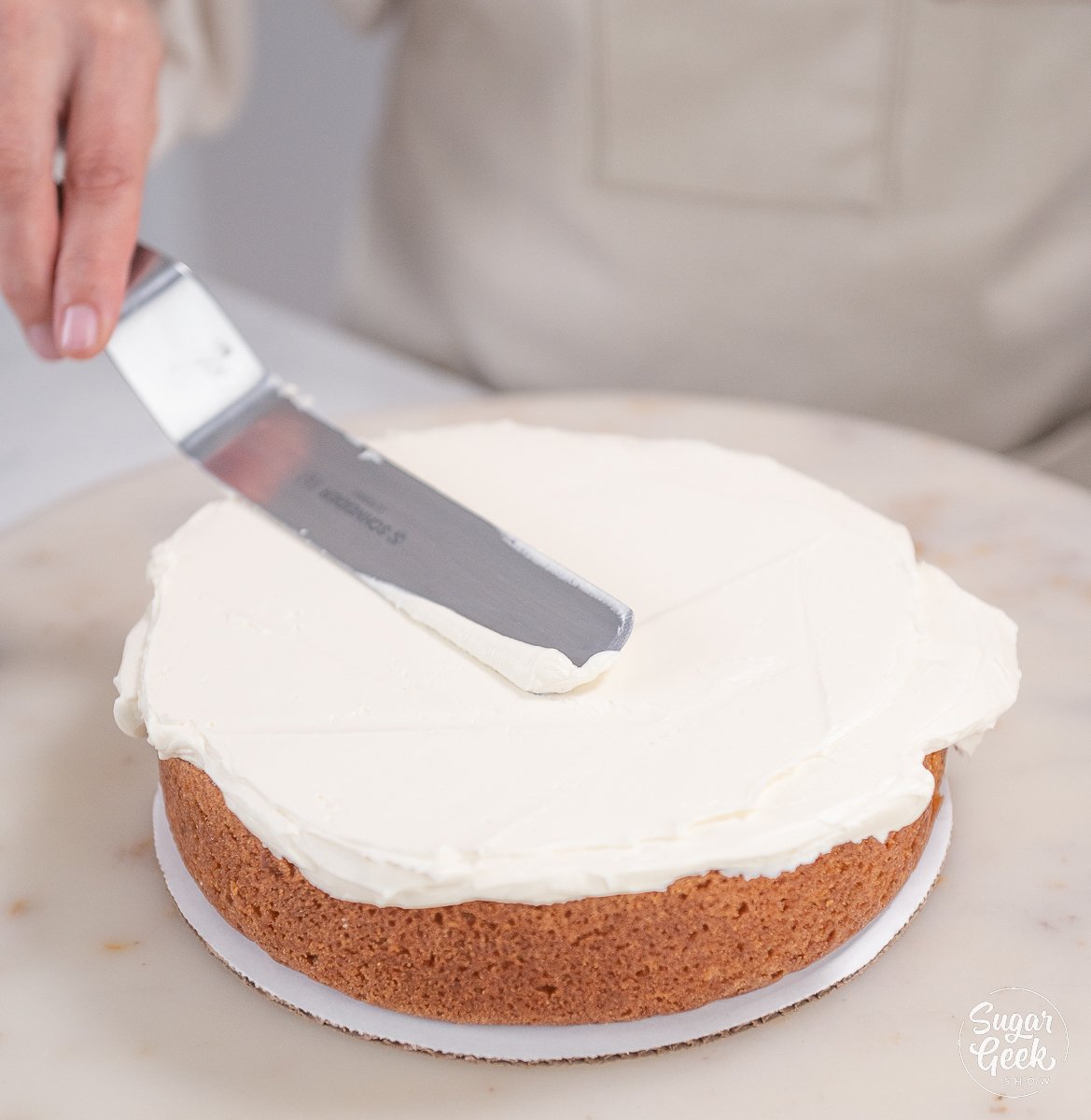 spatula smoothing buttercream on top of cake