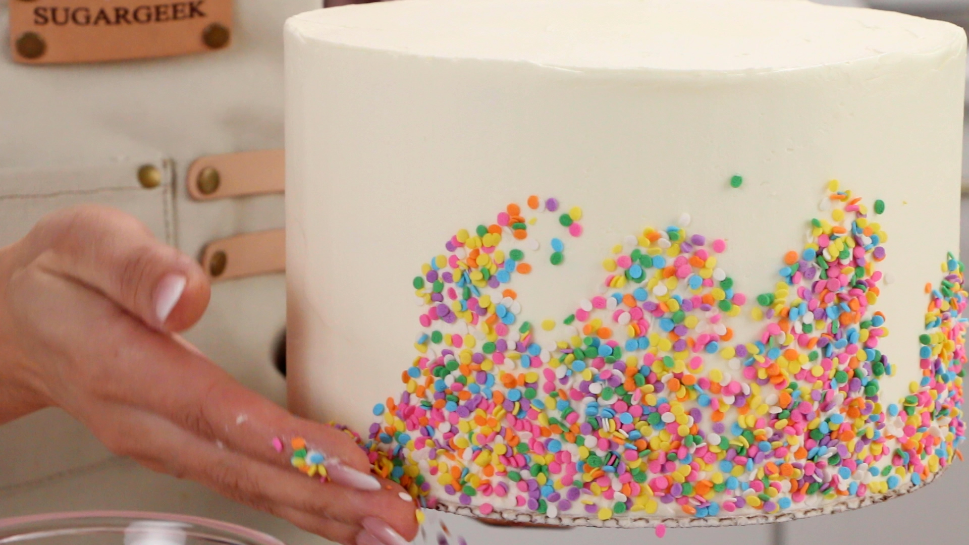 hand covering bottom of a cake with sprinkles