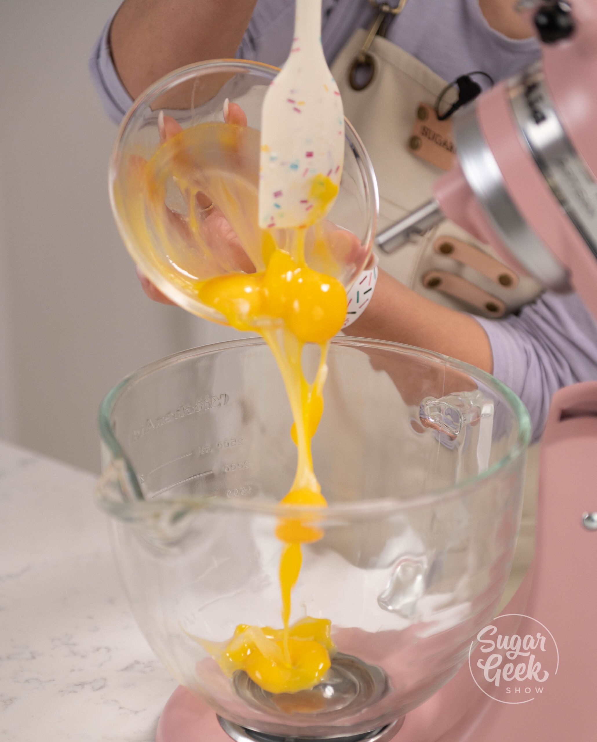 hand holding spatula scraping bowl of eggs into stand mixer