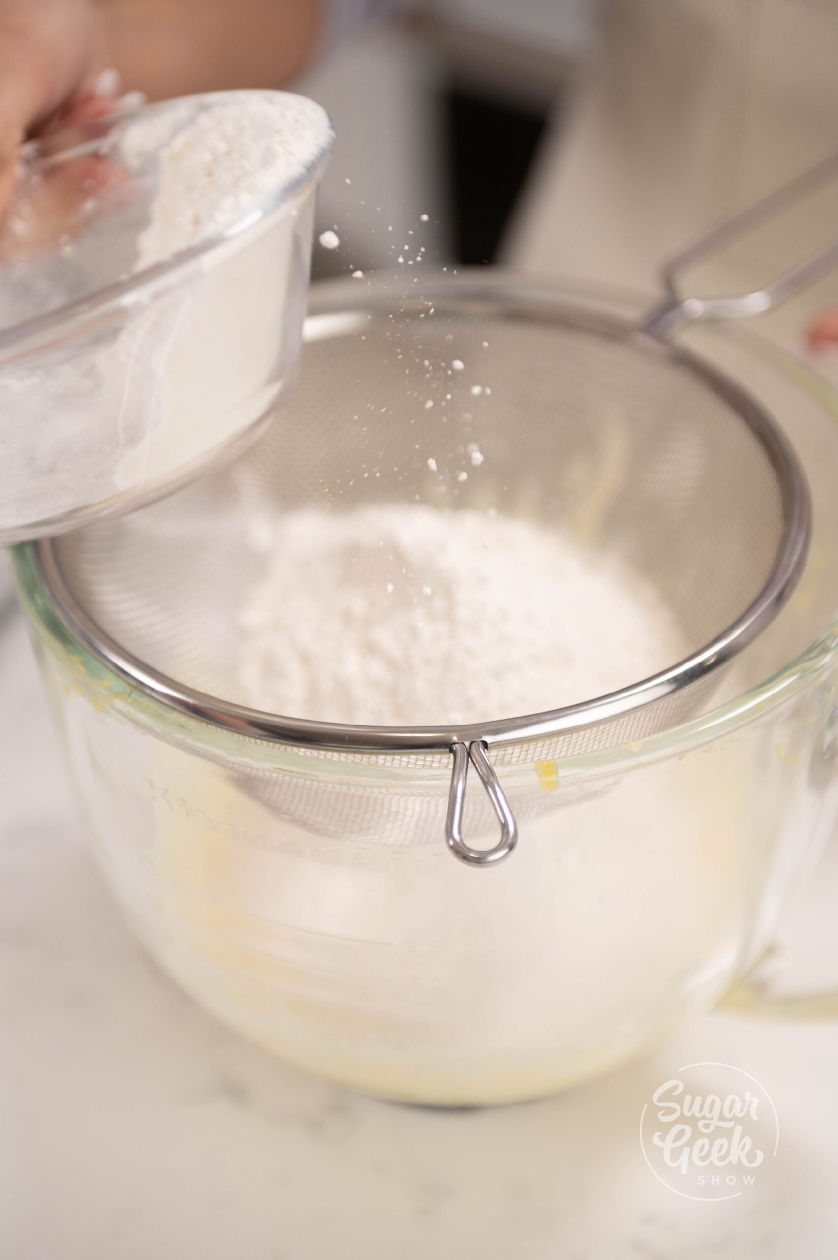 hand pouring bowl of flour over sifter