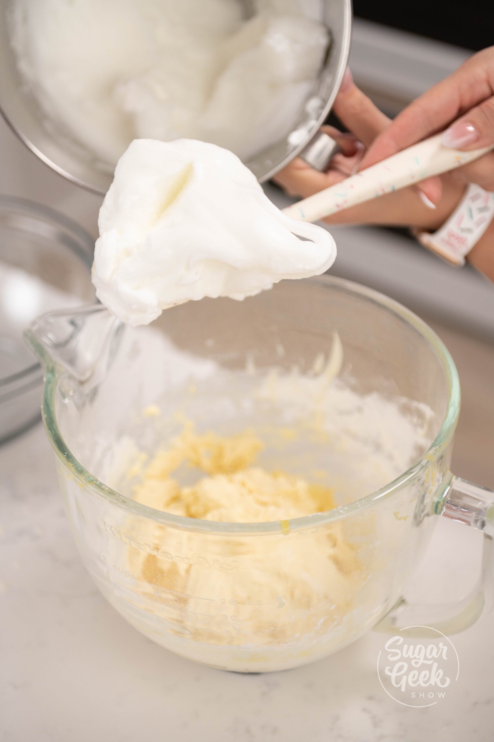 hand holding spatula covered in meringue over bowl of batter