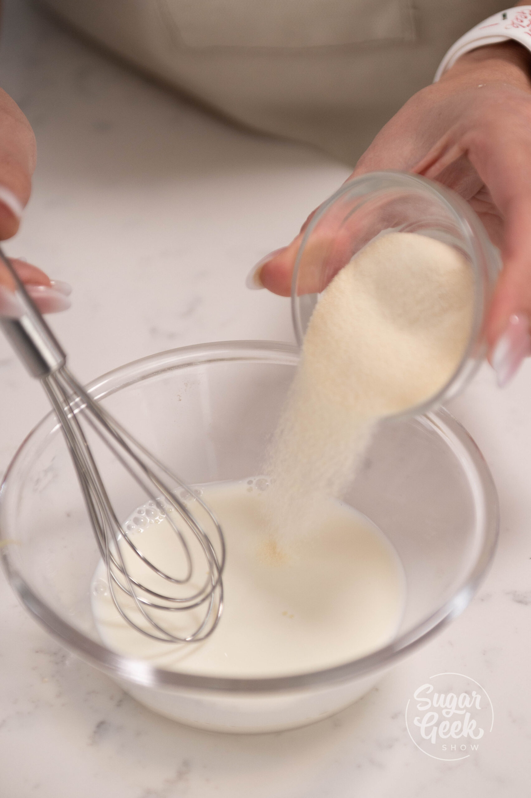 hand holding whisk and bowl of powdered gelatin over bowl of milk