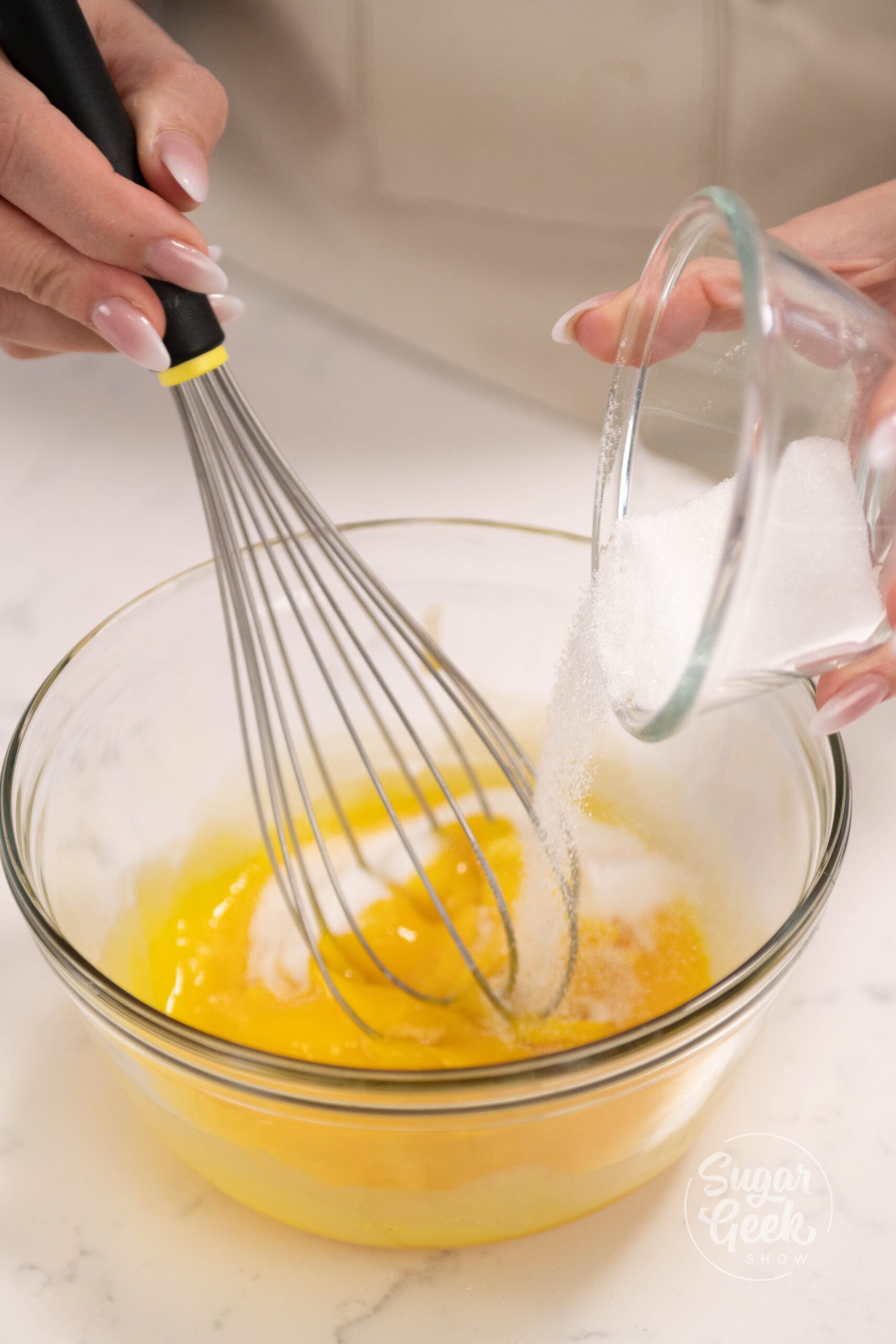 hand pouring sugar into bowl of egg yolks